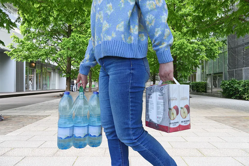 Woman carrying beverage packages with adhesive handles in an urban setting.