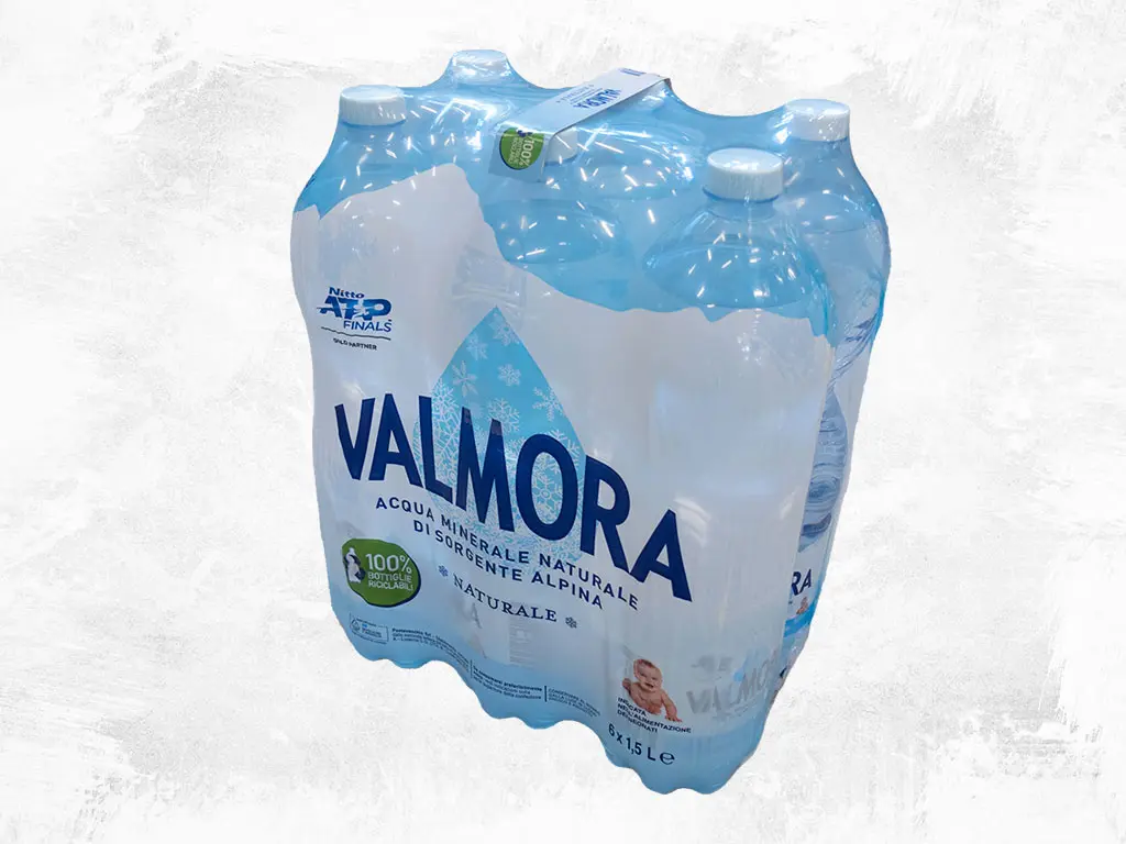 Confezione da 6 bottiglie d'acqua Valmora con maniglia adesiva applicata dall'applicatore di maniglie XHE. Soluzione di packaging innovativa per un trasporto confortevole e una presa sicura, ideale per linee di imbottigliamento veloci.